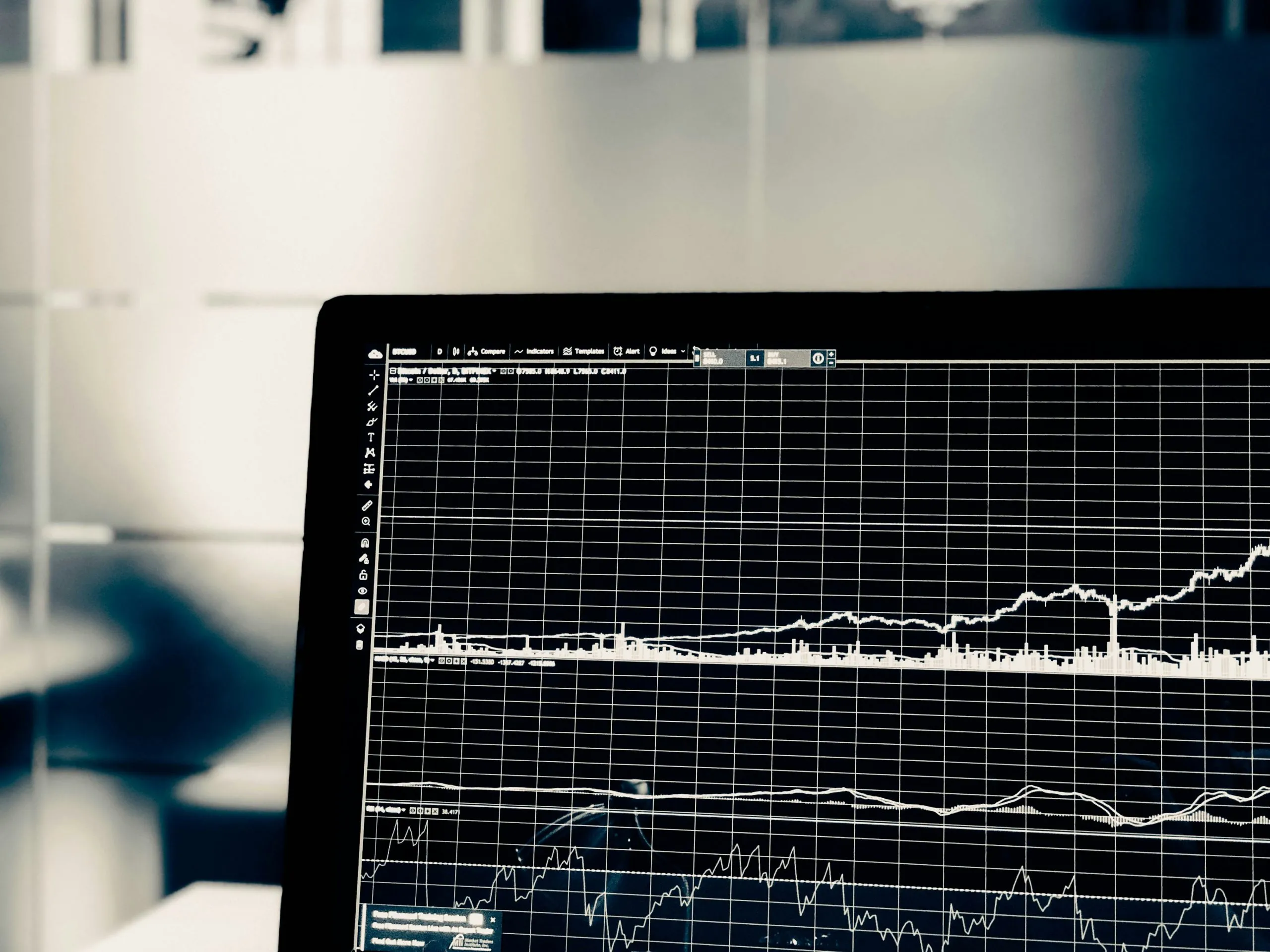 Close-up of a laptop screen displaying a black financial trading chart with white line graphs on a fine grid