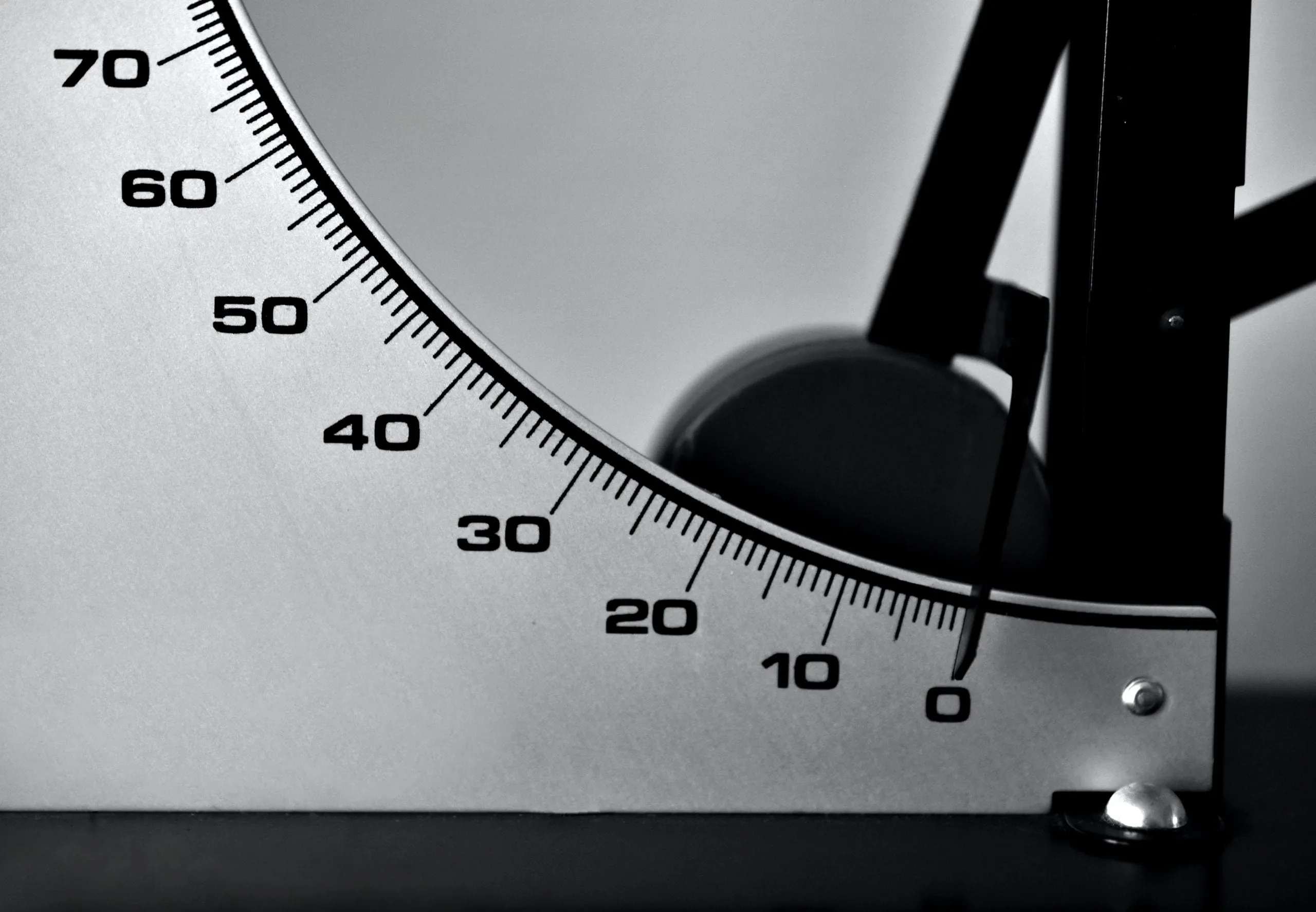 Close-up of a black-and-white measuring gauge with a curved numbered scale from 0 to 70 and a pointer near zero