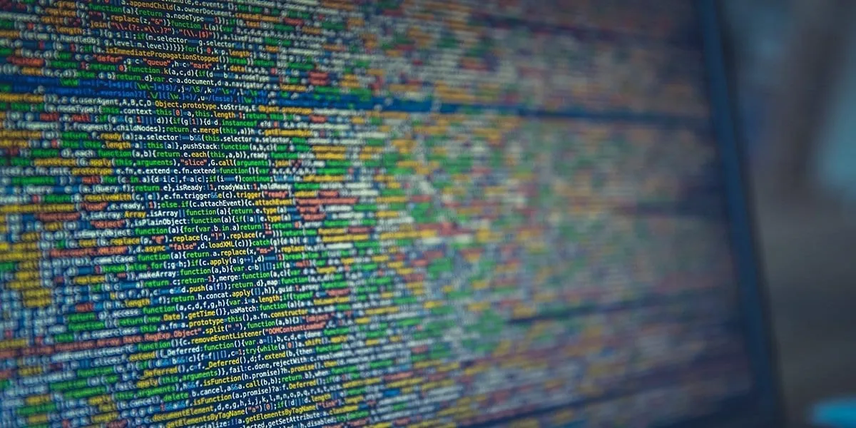 A computer screen filled with dense, colorful minified JavaScript source code viewed at an angle