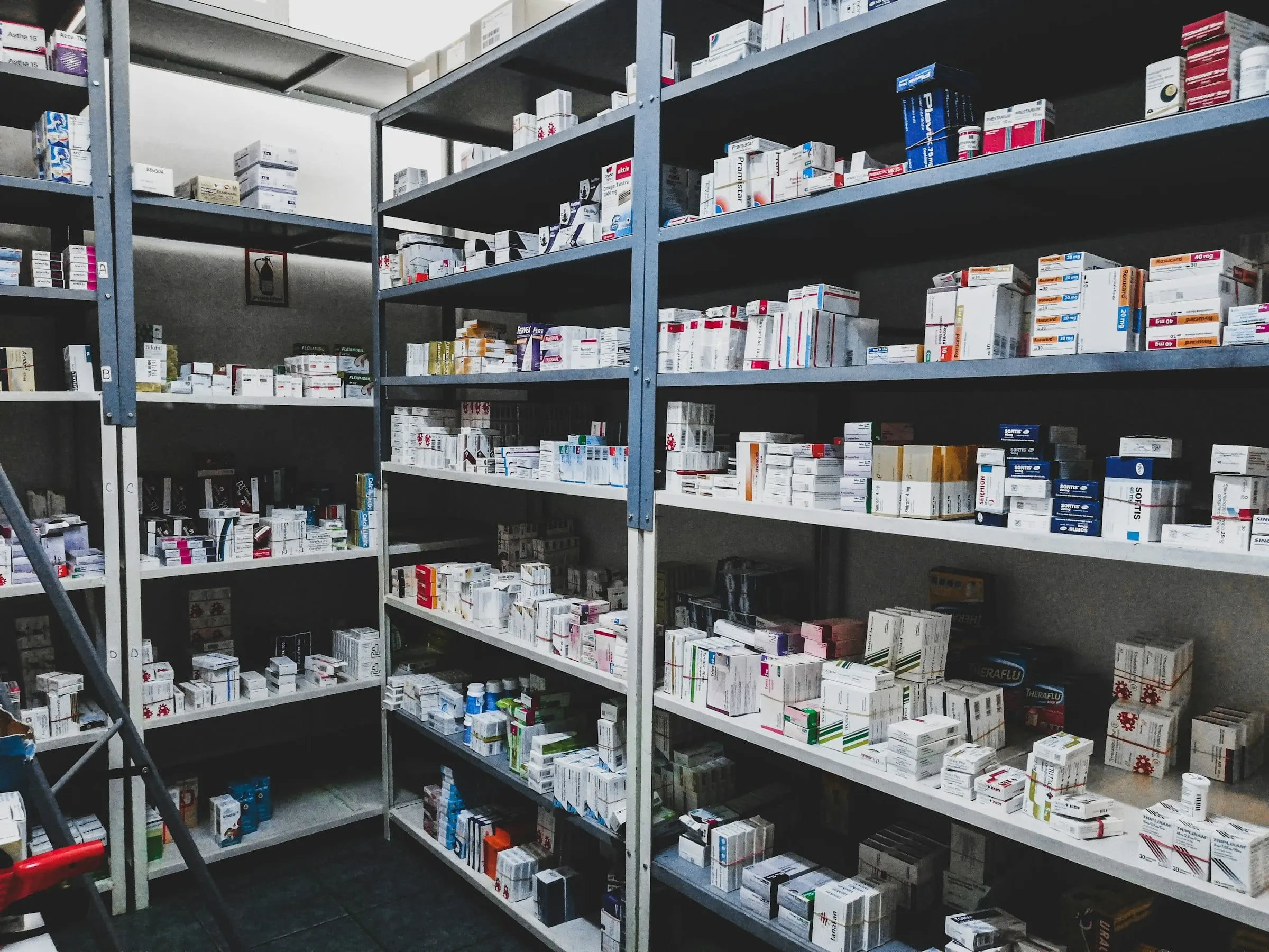 Pharmacy stockroom with metal shelving packed full of boxed medications and product cartons