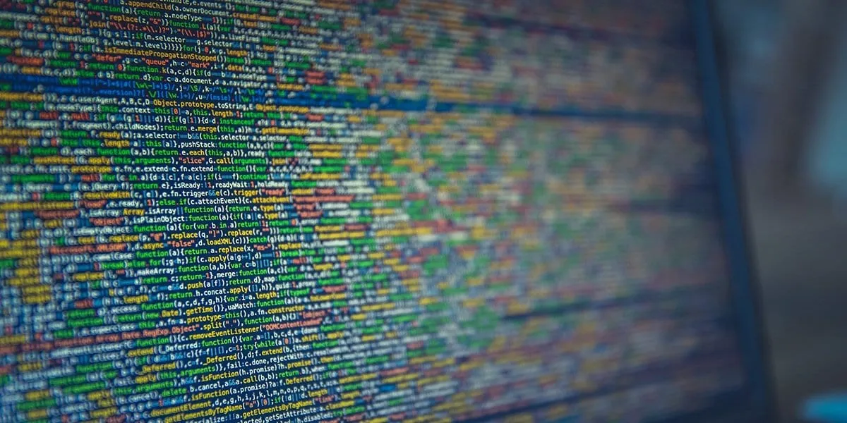 A computer screen filled with dense, colorful minified JavaScript source code viewed at an angle