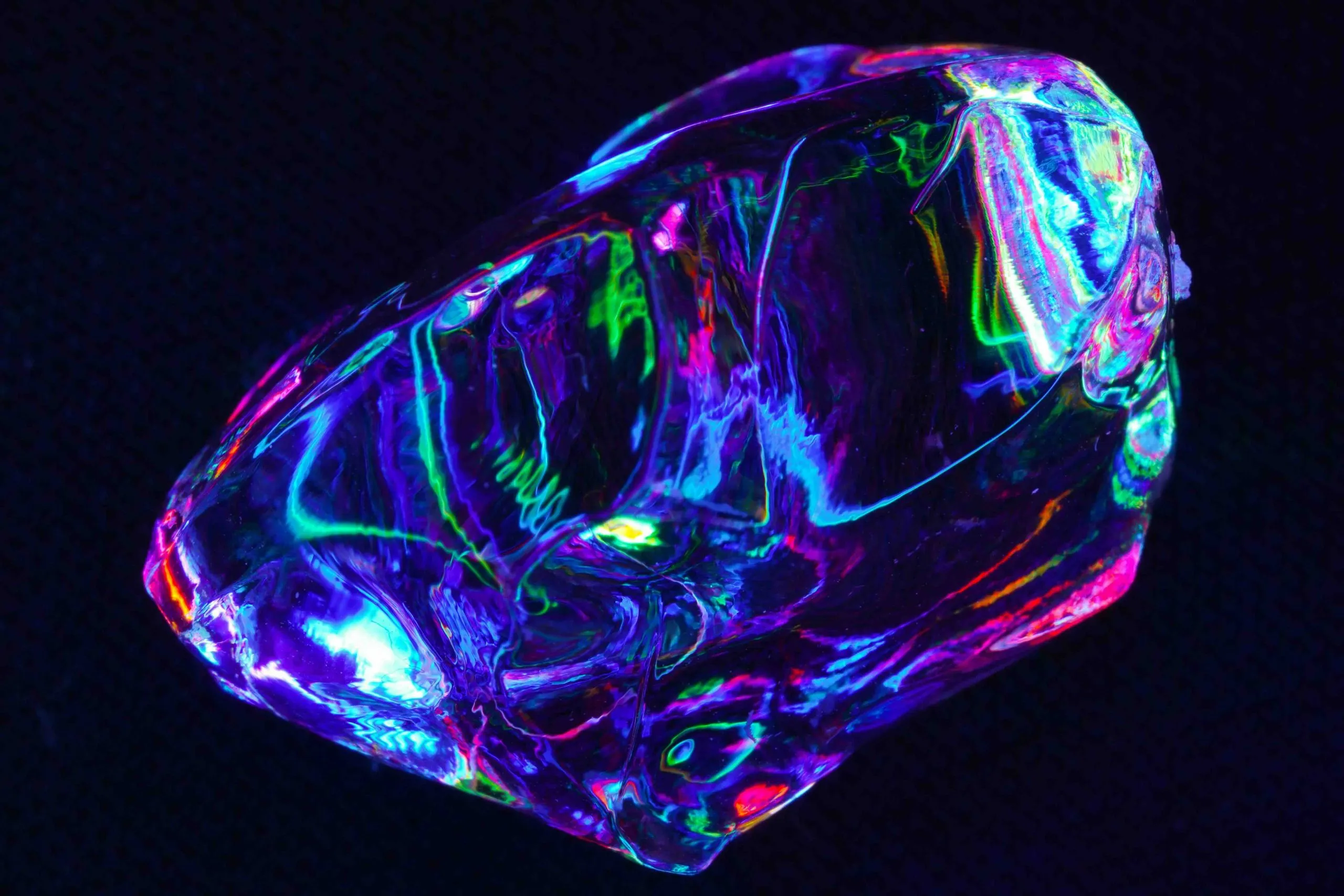 Clear crystalline shard glowing with iridescent blue, green and pink light against a black background