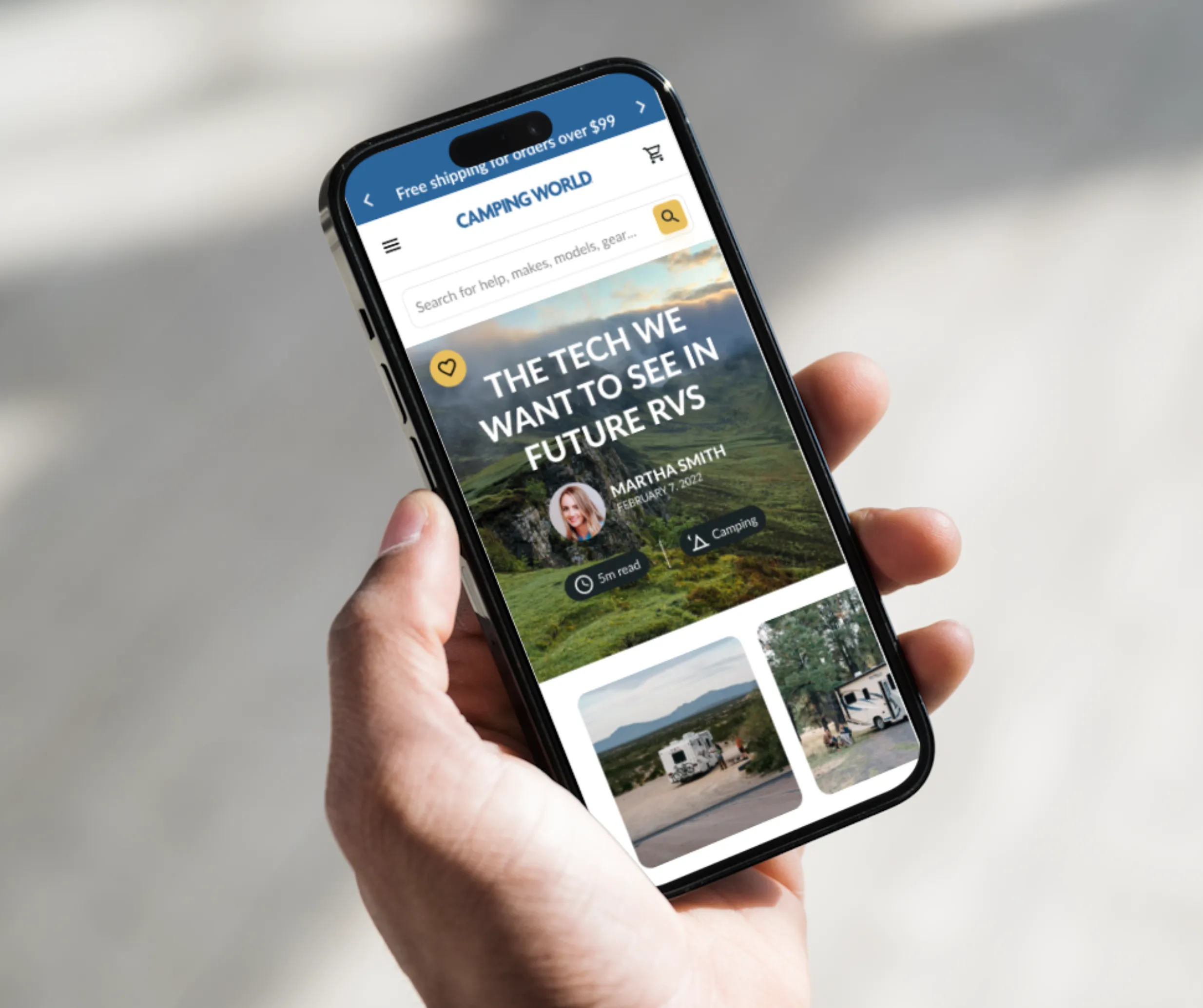 Hand holding a phone showing the Camping World mobile site with a future-of-RVs article over a mountain landscape