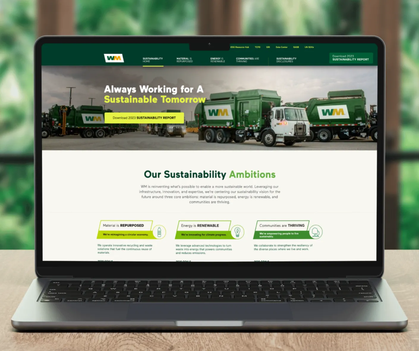 Laptop mockup of WM sustainability site homepage with green garbage trucks and 'Always Working for a Sustainable Tomorrow' headline