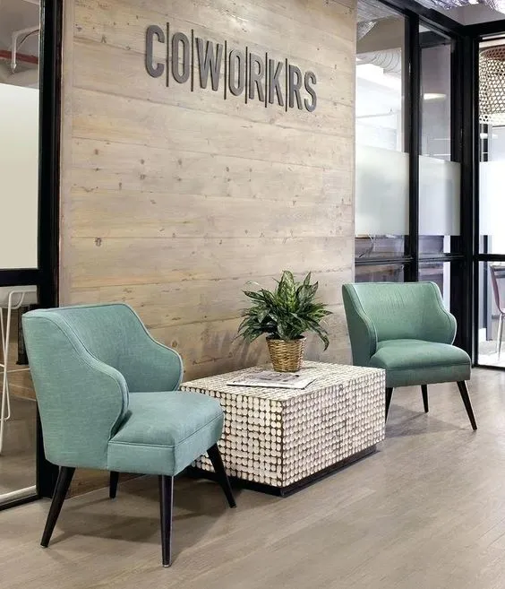 Coworking interior inspiration — teal accent chairs and plant by a wood feature wall reading 'COWORKS'