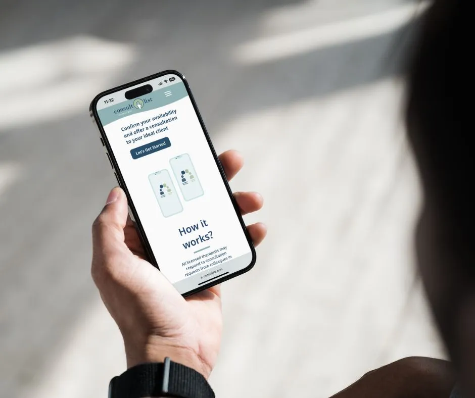 An over the shoulder view of a person holding an iPhone with the consultlist.com marketing site homepage visible on the screen